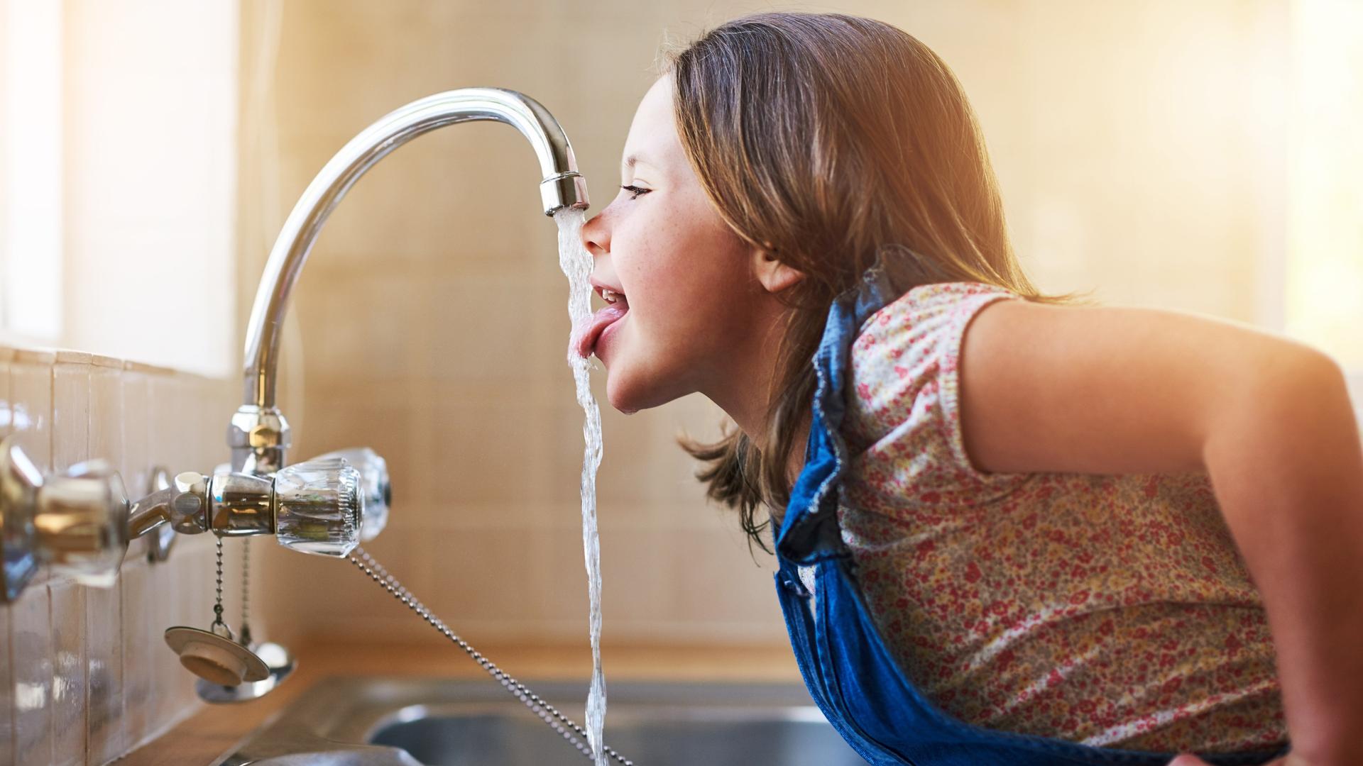 Ein Mädchen trinkt direkt aus dem Wasserhahn