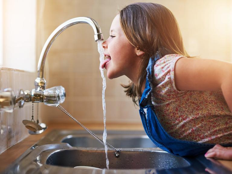 Ein Mädchen trinkt direkt aus dem Wasserhahn