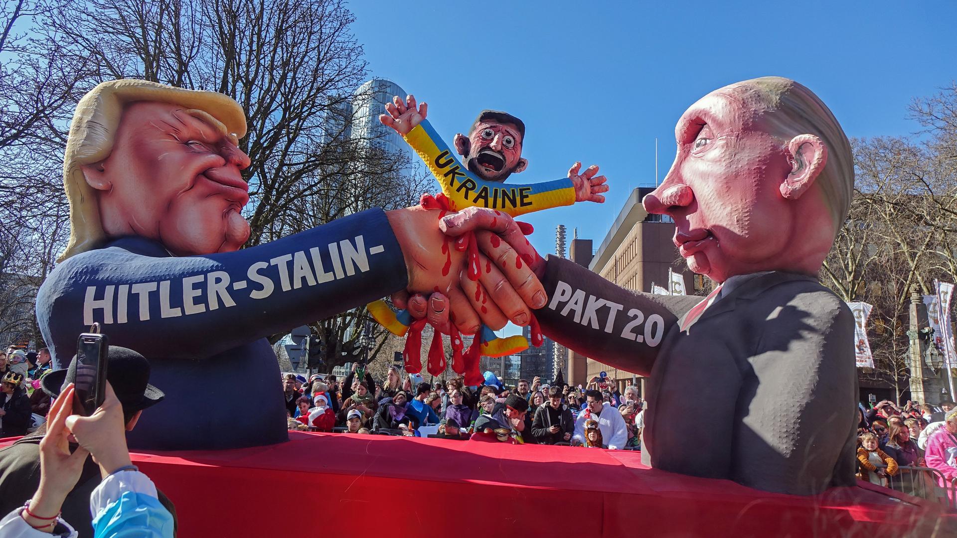 Ein Motivwagen auf dem Rosenmontagszug in Düsseldorf zeigt Donald Trump und Wladimir Putin. Sie besiegeln mit einem Handschlag einen "Hitler-Stalin-Pakt 2.0" auf Kosten der Ukraine. Ein Motivwagen auf dem Rosenmontagszug in Düsseldorf zeigt Donald Trump und Wladimir Putin. Sie besiegeln mit einem Handschlag einen "Hitler-Stalin-Pakt 2.0" auf Kosten der Ukraine.