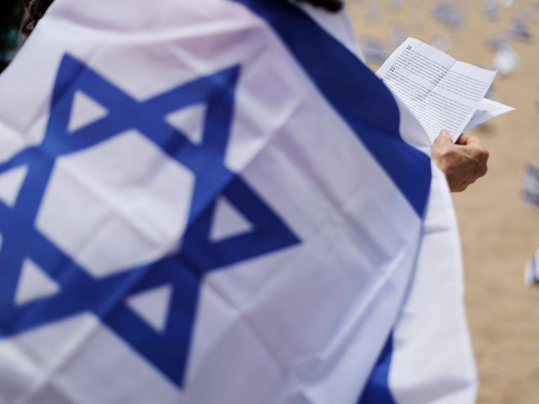 Ein Mensch betet in eine Israel-Fahne gehüllt.