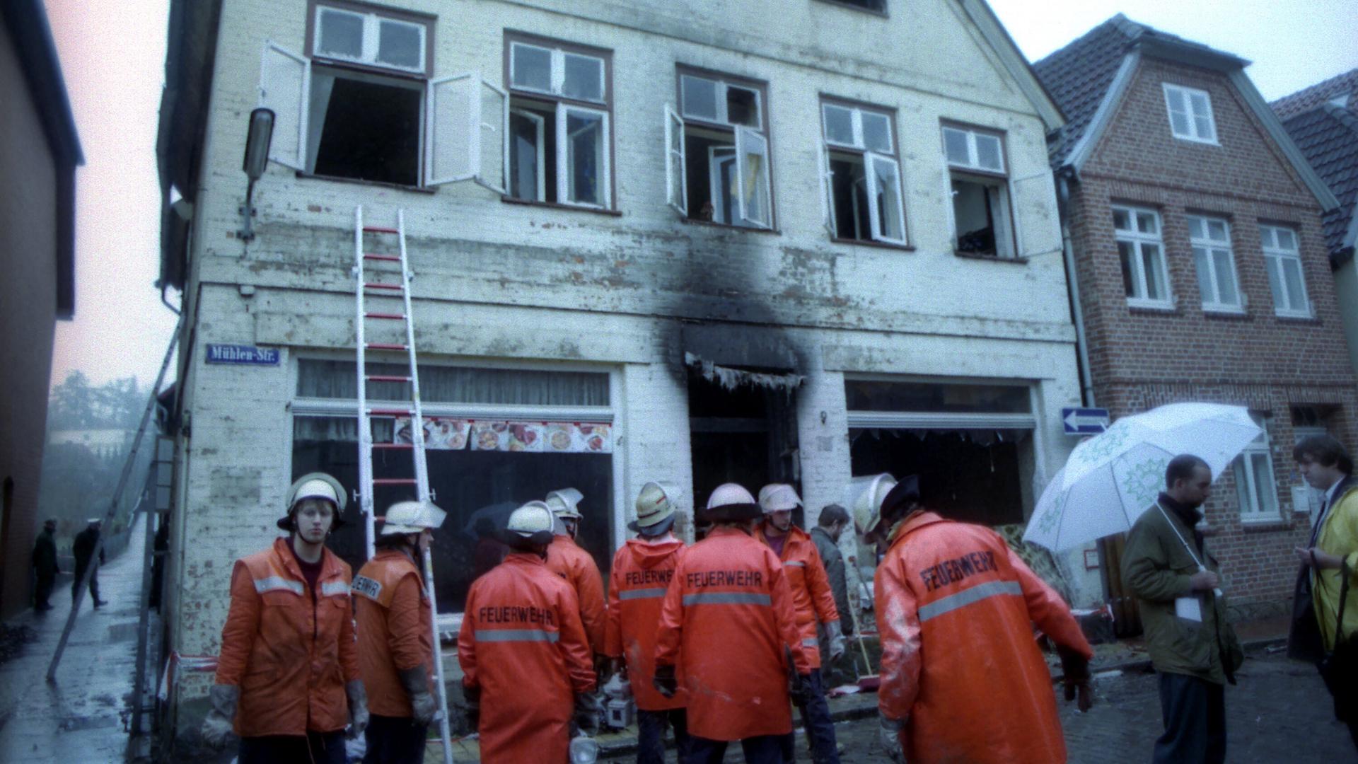 Eine Gruppe Feuerwehrleute steht am Montagmorgen vor dem ausgebrannten Haus in Mölln.