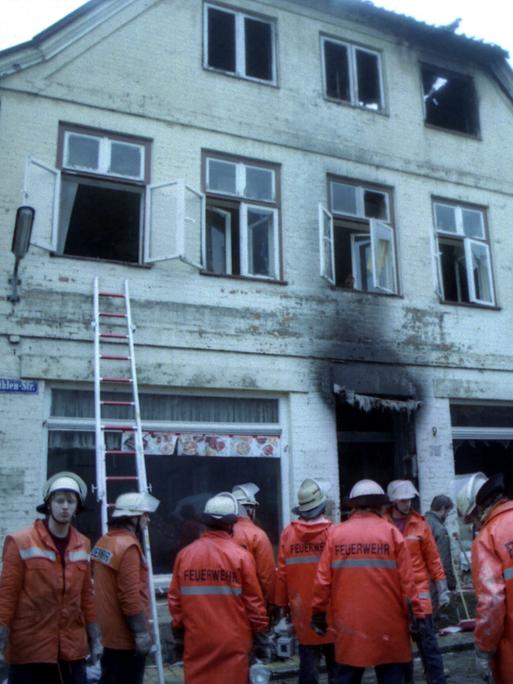 Eine Gruppe Feuerwehrleute steht am Montagmorgen vor dem ausgebrannten Haus in Mölln.