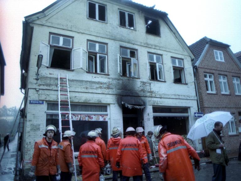 Eine Gruppe Feuerwehrleute steht am Montagmorgen vor dem ausgebrannten Haus in Mölln.