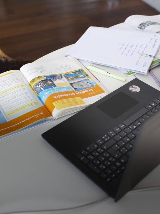 Zu sehen ist ein häuschlicher Schreibtisch mit einem Laptop und Schulbüchern und Lernmaterialien.