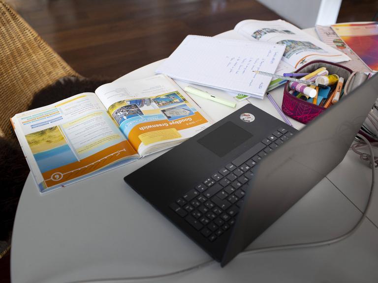 Zu sehen ist ein häuschlicher Schreibtisch mit einem Laptop und Schulbüchern und Lernmaterialien.