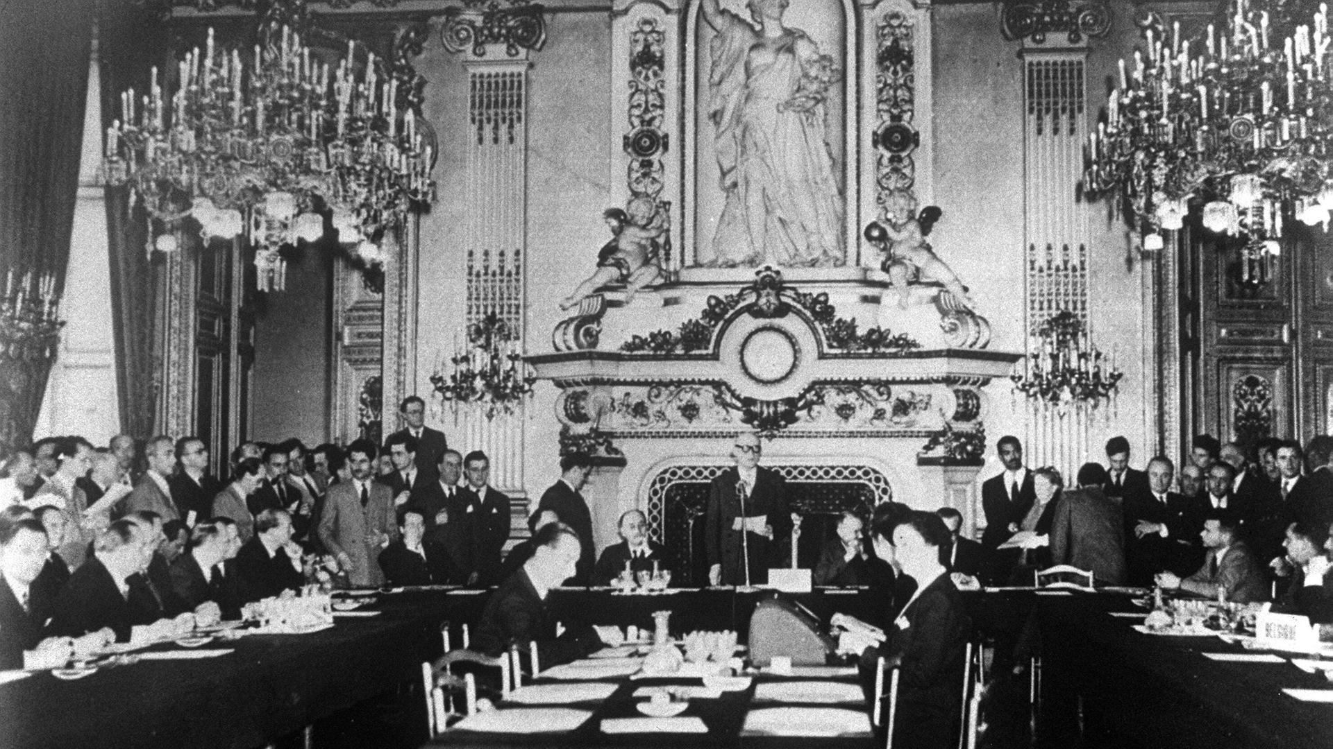 Eine schwarz-weiß Aufnahme des französischen Außenminister Robert Schuman, der im Uhrensaal des Außenministeriums am Quai d'Orsay in Paris vor der Nationalversammlung eine Rede hält