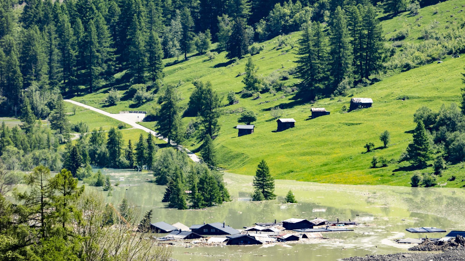 Das Foto zeigt das überflutete Dorf Blatten im Schweizer Lötschental. Von den Häusern sind nur noch Dächer zu sehen. Im Vordergrund ist eine Gerölllawine. Das Foto zeigt das überflutete Dorf Blatten im Schweizer Lötschental. Von den Häusern sind nur noch Dächer zu sehen. Im Vordergrund ist eine Gerölllawine.