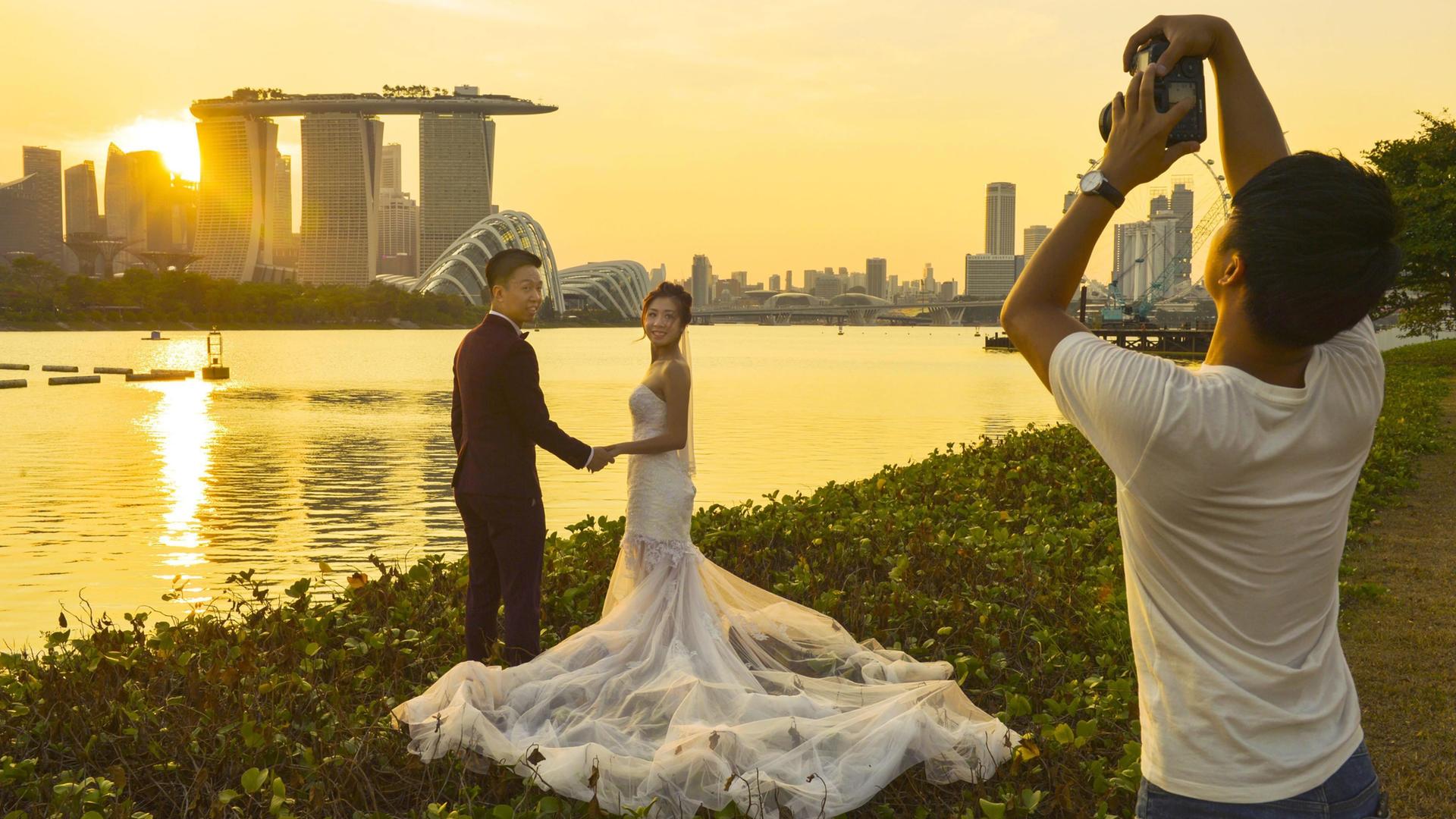 Ein Hochzeitspaar postiert für einen Fotografen vor der Bucht des Jachthafens von Singapur. Ein Hochzeitspaar postiert für einen Fotografen vor der Bucht des Jachthafens von Singapur.