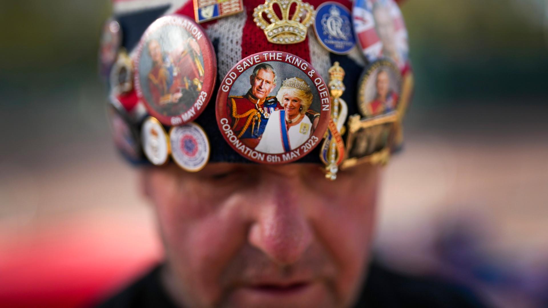 Ein Brite trägt wenige Tage vor der Krönung von King Charles III. eine Mütze, die mit Stickern die britische Monarchie feiert.