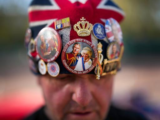 Ein Brite trägt wenige Tage vor der Krönung von King Charles III. eine Mütze, die mit Stickern die britische Monarchie feiert.