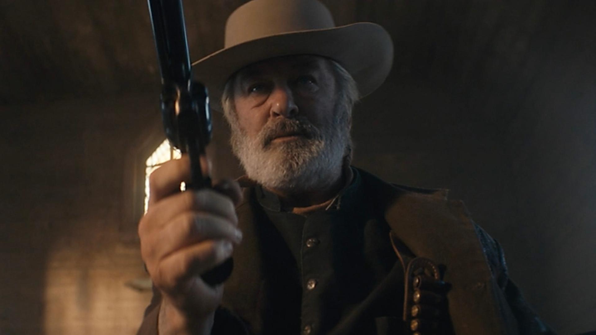 In einer Szene des US-Western "Rust" hält der Schauspieler Alec Baldwin einen Revolver auf die Kamera gerichtet. Er hat Westernkleidung an und einen Cowboy-Hut auf.