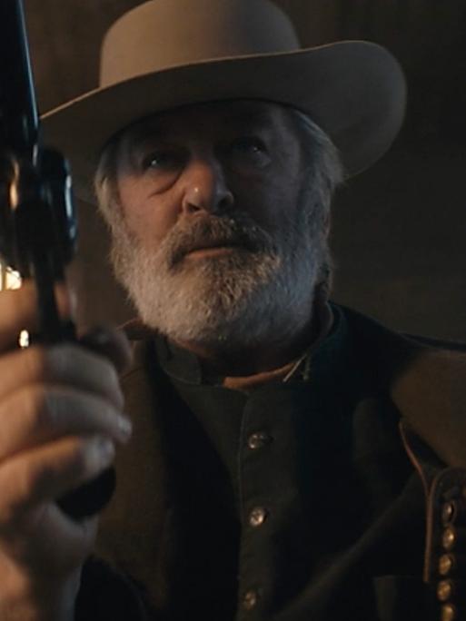 In einer Szene des US-Western "Rust" hält der Schauspieler Alec Baldwin einen Revolver auf die Kamera gerichtet. Er hat Westernkleidung an und einen Cowboy-Hut auf.