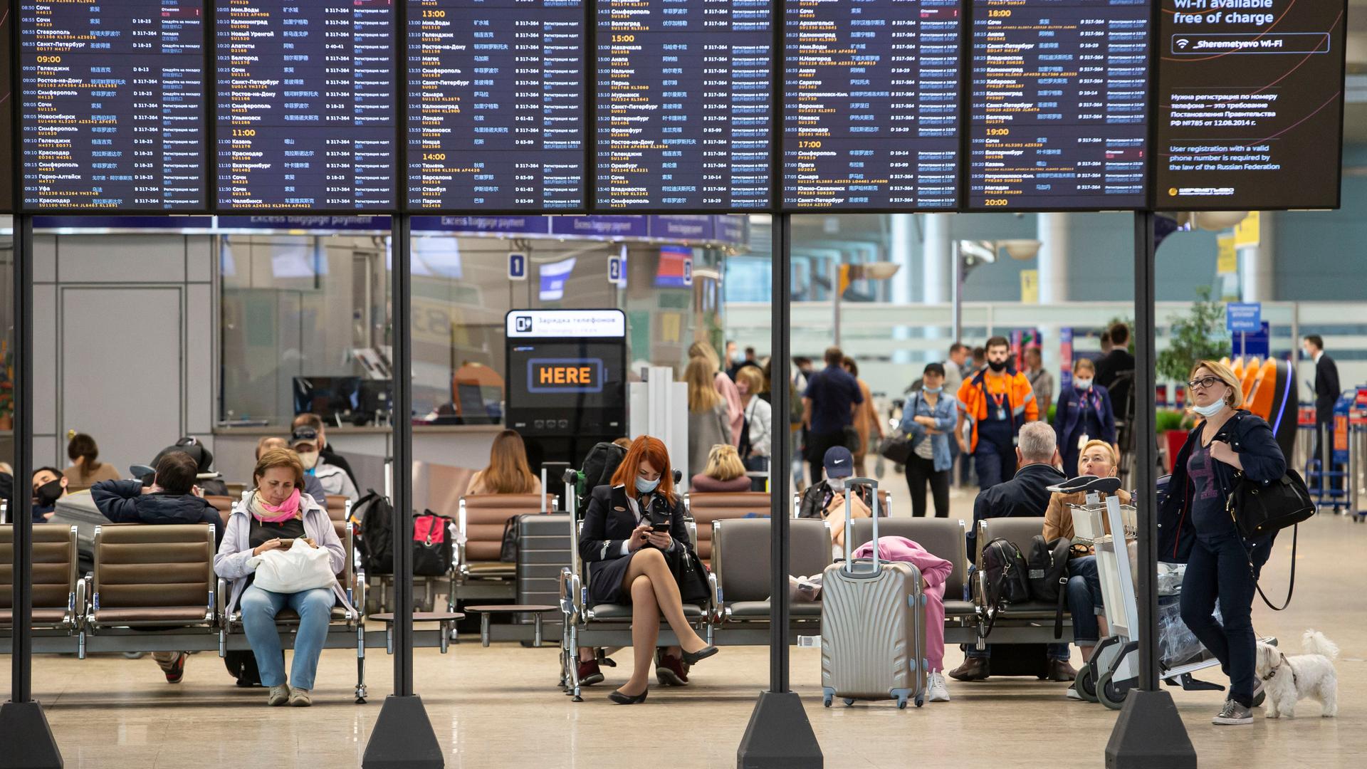 Passagiere sitzen auf dem internationalen Flughafen Scheremetjewo unter einer Fluginformationstafel. 