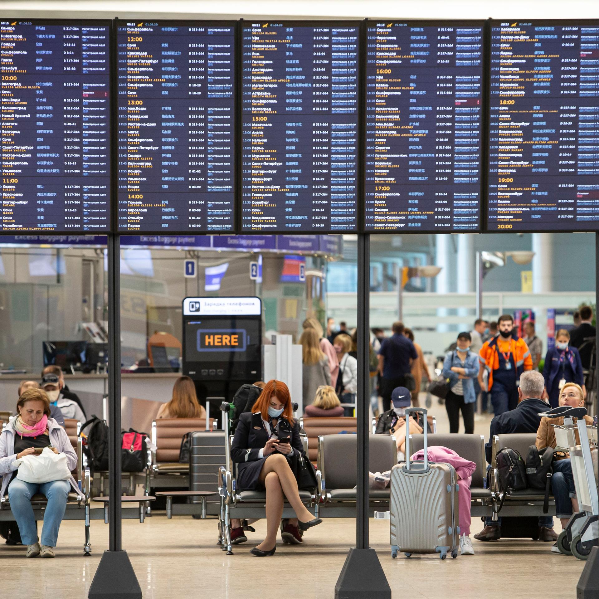 Passagiere sitzen auf dem internationalen Flughafen Scheremetjewo unter einer Fluginformationstafel. 