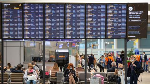 Passagiere sitzen auf dem internationalen Flughafen Scheremetjewo unter einer Fluginformationstafel. 
