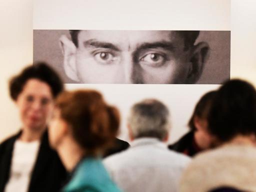 Eine Fotografie von Kafkas Augenpartie starrt Leute in einer Galerie an.