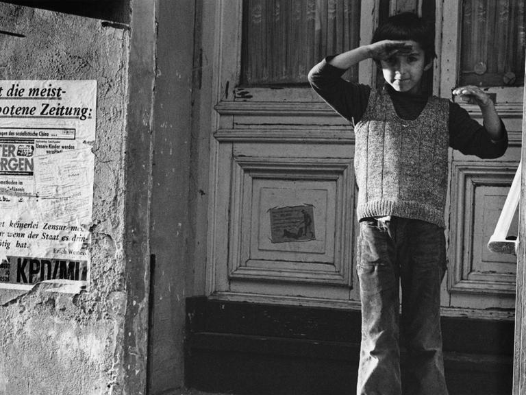 Ein türkischer Junge in Berlin-Kreuzberg 1976 steht vor einer Haustür und hält seine rechte Hand als Schutz gegen die Sonne über die Augen.