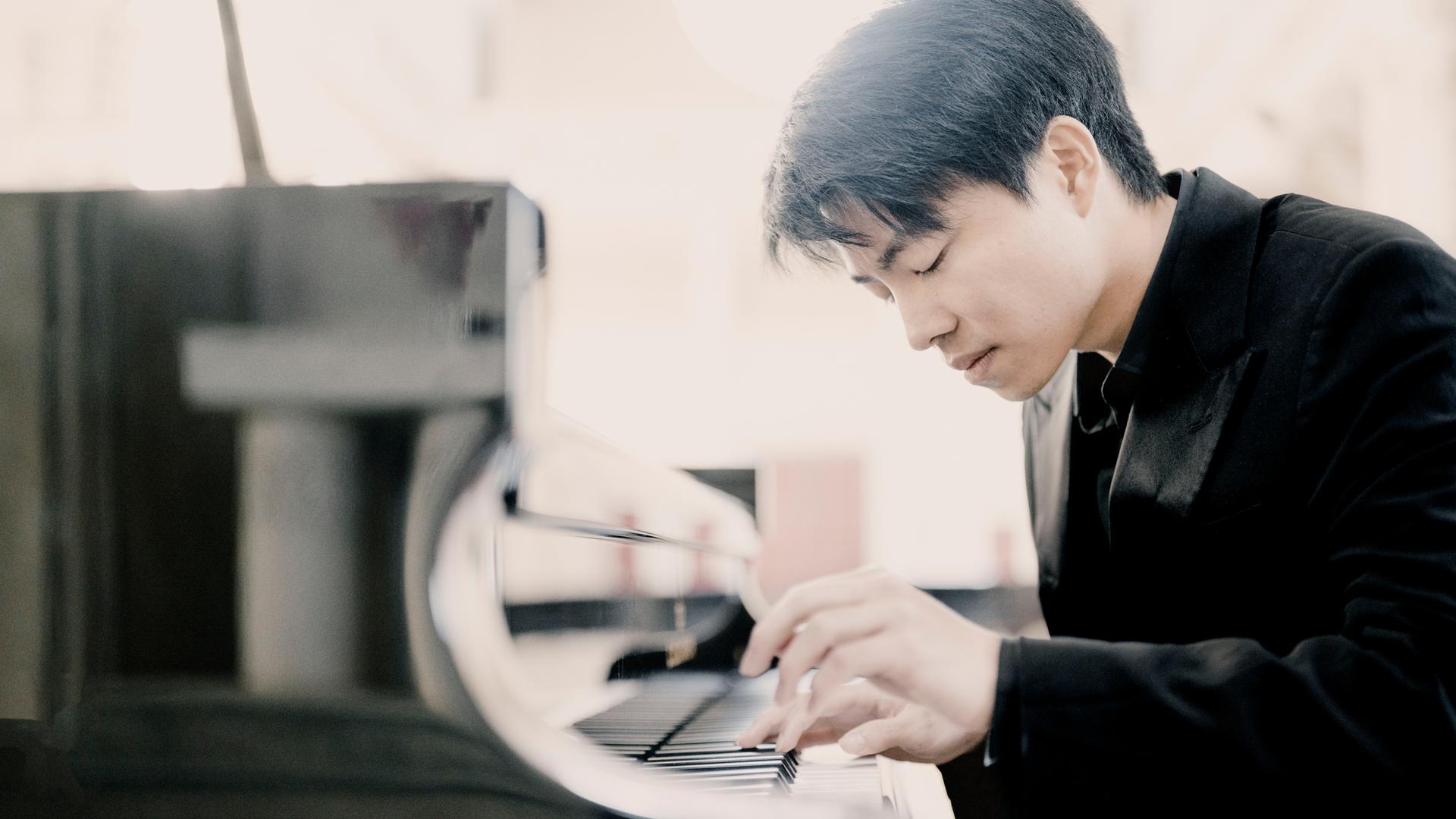 Eine junger Mann mit kurzen schwarzen Haaren beugt sich über eine Klaviertastatur. Die Hände auf den Tasten, er spielt. Es ist der Pianist Kit Armstrong.