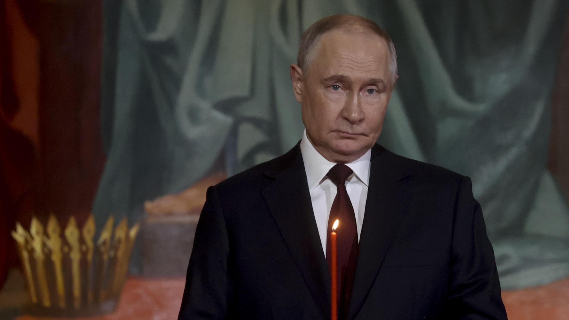 Präsident Putin steht in einer Kirche in dunklem Anzug und hält eine brennende Kerze in der Hand, er schaut sehr ernst. Präsident Putin steht in einer Kirche in dunklem Anzug und hält eine brennende Kerze in der Hand, er schaut sehr ernst.