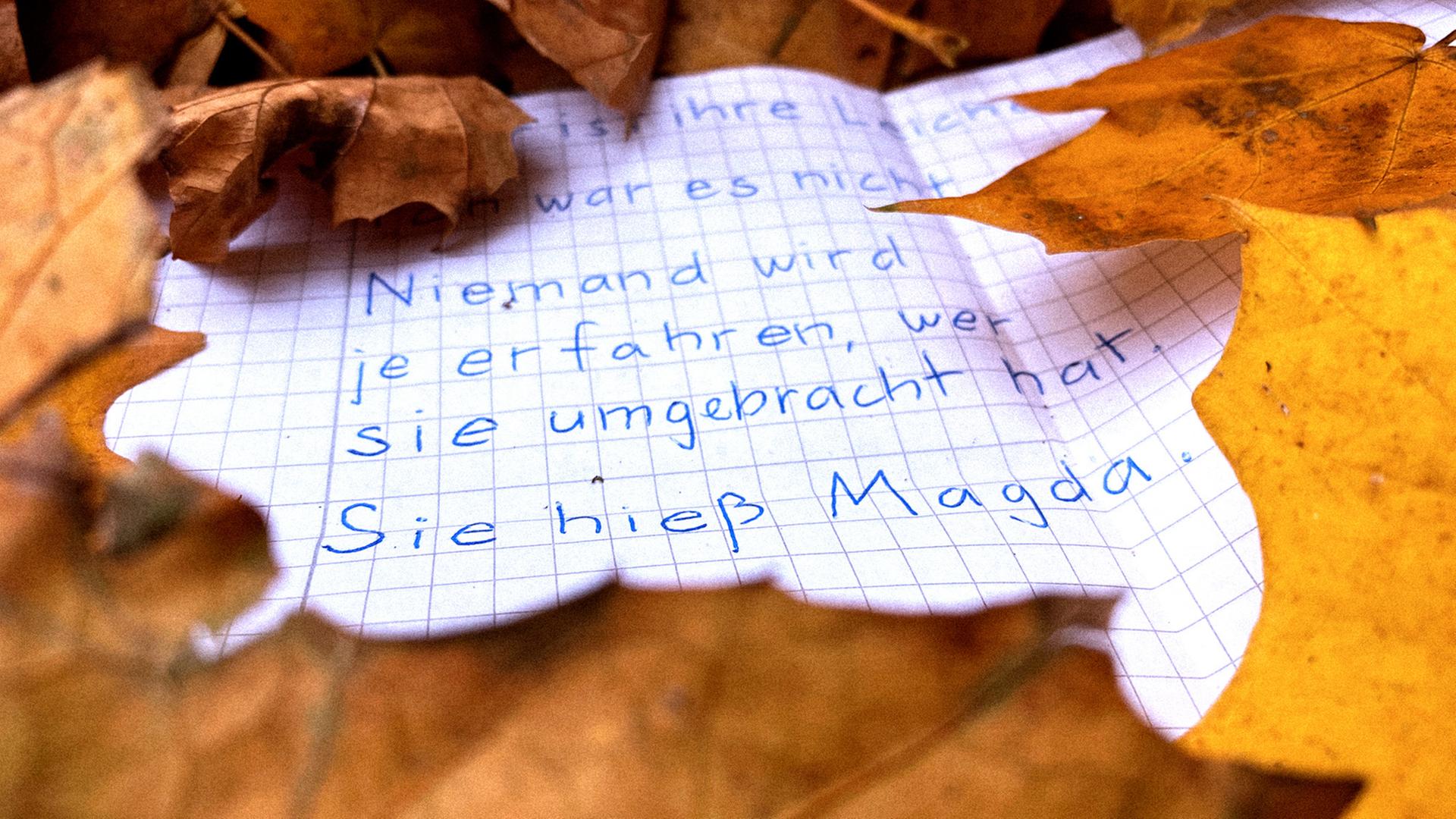 Ein beschrifteter Zettel liegt im Herbstlaub. Darauf ist zu lesen: "Niemand wird es je erfahren, wer sie umgebracht hat. Sie hieß Magda."