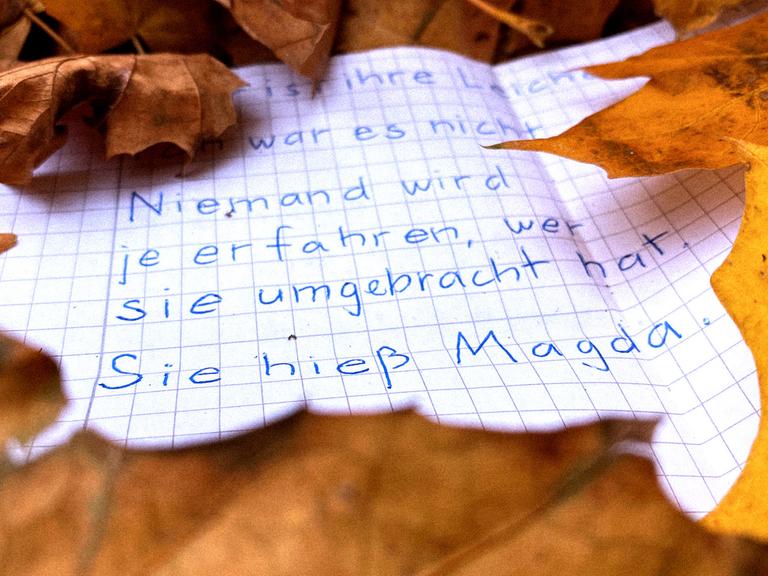 Ein beschrifteter Zettel liegt im Herbstlaub. Darauf ist zu lesen: "Niemand wird es je erfahren, wer sie umgebracht hat. Sie hieß Magda."