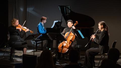 Vier Musiker sitzen auf der Bühne und spielen unter kontrastreicher Bühnenbeleuchtung ein Stück.