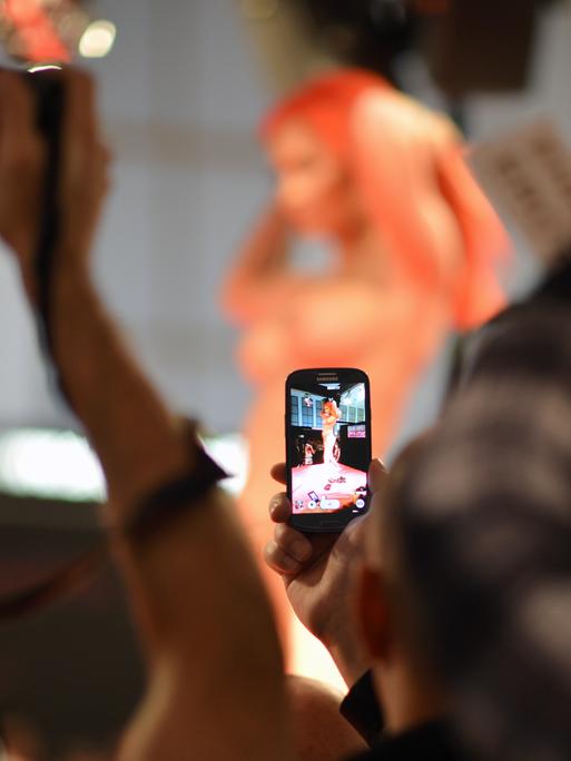 Menschen filmen und fotografieren eine Frau, die sich nackt auf einer Bühne zeigt.