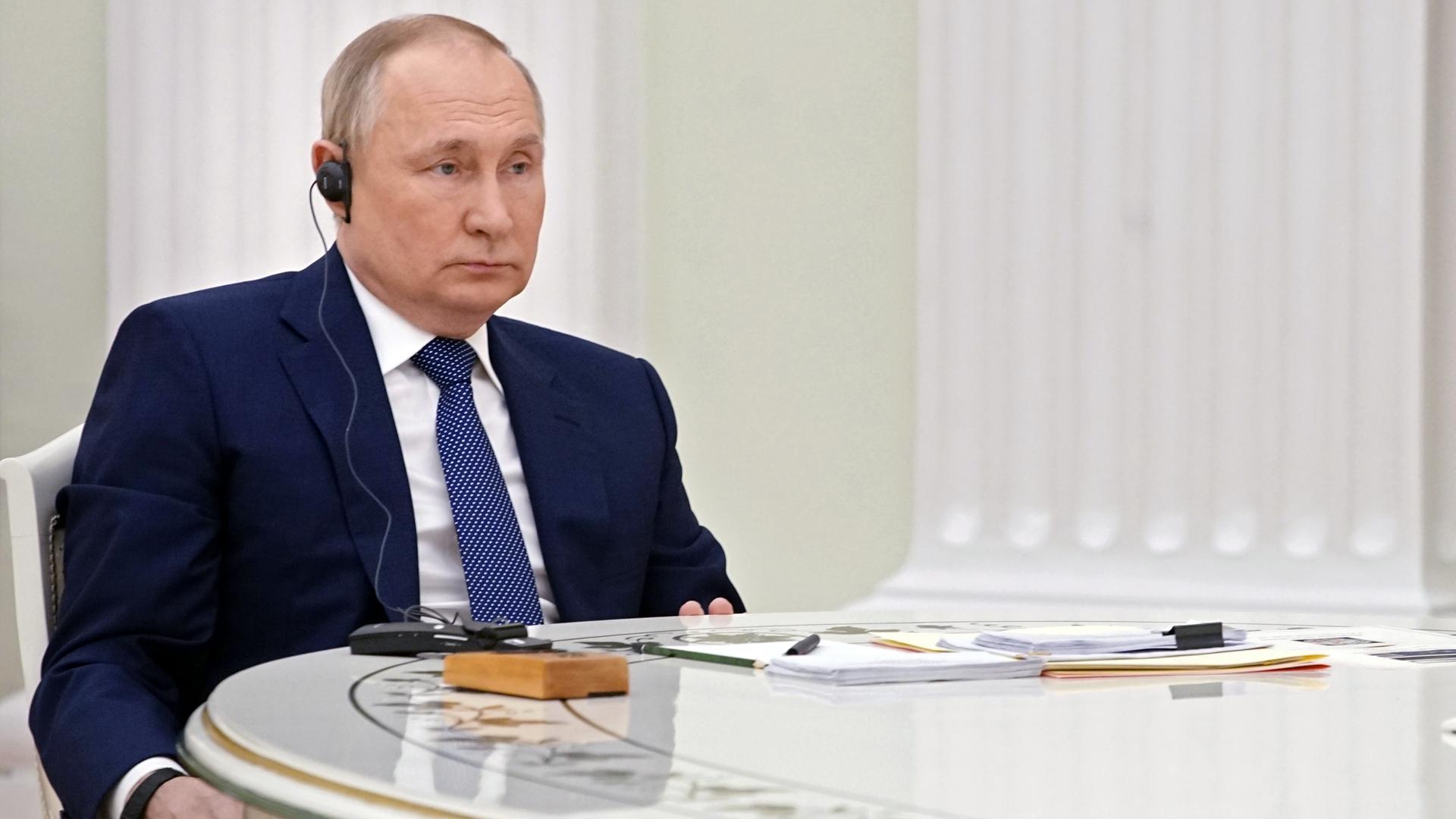 Wladimir Putin sitzt an einem Tisch und hört zu.