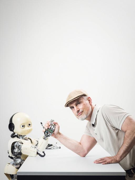 Ein Mann mittleren Alters (Informatiker und IDSIA Direktor Jürgen Schmidbauer) posiert beim Armdrücken mit dem humanoiden iCub-Roboter im Institut für künstliche Intelligenz IDSIA in Manno bei Lugano. 