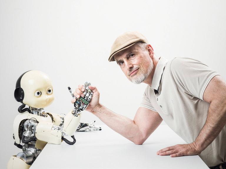 Ein Mann mittleren Alters (Informatiker und IDSIA Direktor Jürgen Schmidbauer) posiert beim Armdrücken mit dem humanoiden iCub-Roboter im Institut für künstliche Intelligenz IDSIA in Manno bei Lugano. 