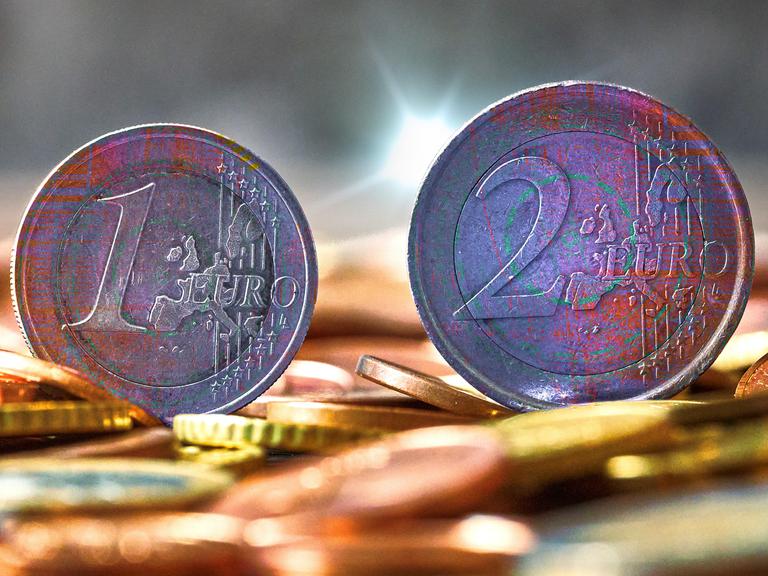 Fotomontage: zwei Euromünzen im Fokus, dahinter digitales Rauschen. Symbolbild für die anstehende Einführung des digitalen Euro.