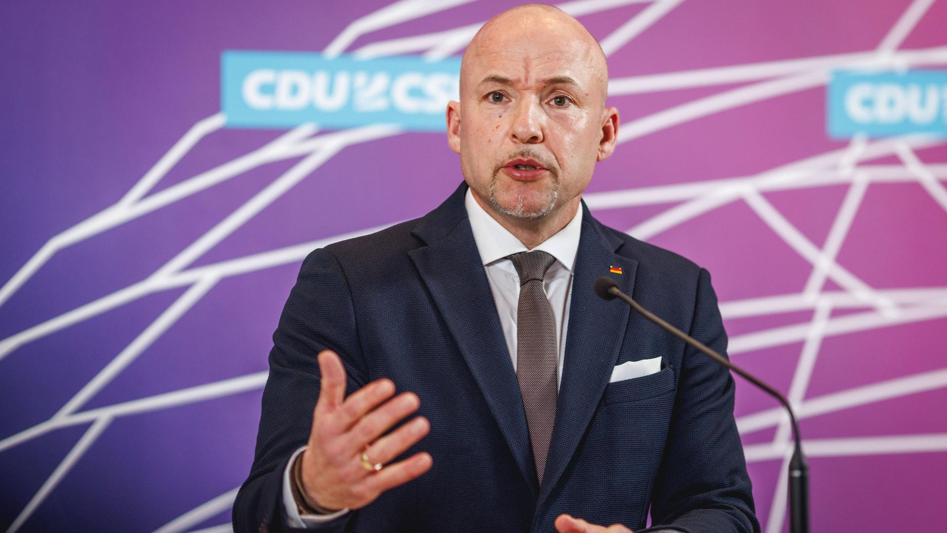 Das Foto zeigt den CSU-Politiker Alexander Hoffmann. Er steht vor einer Wand mit der Aufschrift "CDU/CSU" und gestikuliert mit der rechten Hand in Richtung Kamera (Archivbild vom April 2024).