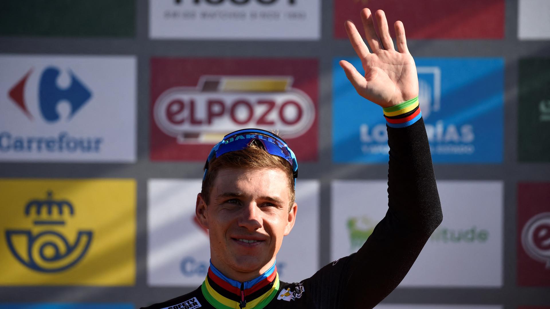 Der belgische Radprofi Remco Evenepoel steht bei der Siegerehrung der Spanien-Rundfahrt auf dem Podest und winkt mit der linken Hand.