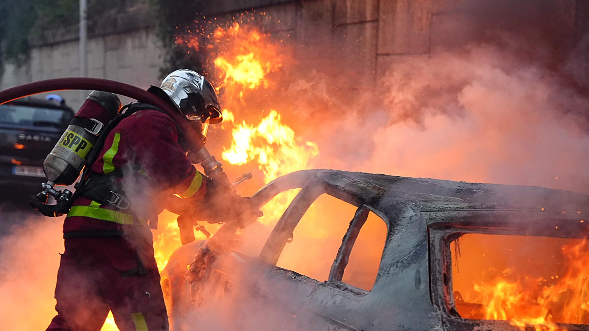 Ein Feuerwehrmann löscht ein brennendes Fahrzeug nach Ausschreitungen im Pariser Vorort Nanterre. Ein Feuerwehrmann löscht ein brennendes Fahrzeug nach Ausschreitungen im Pariser Vorort Nanterre.