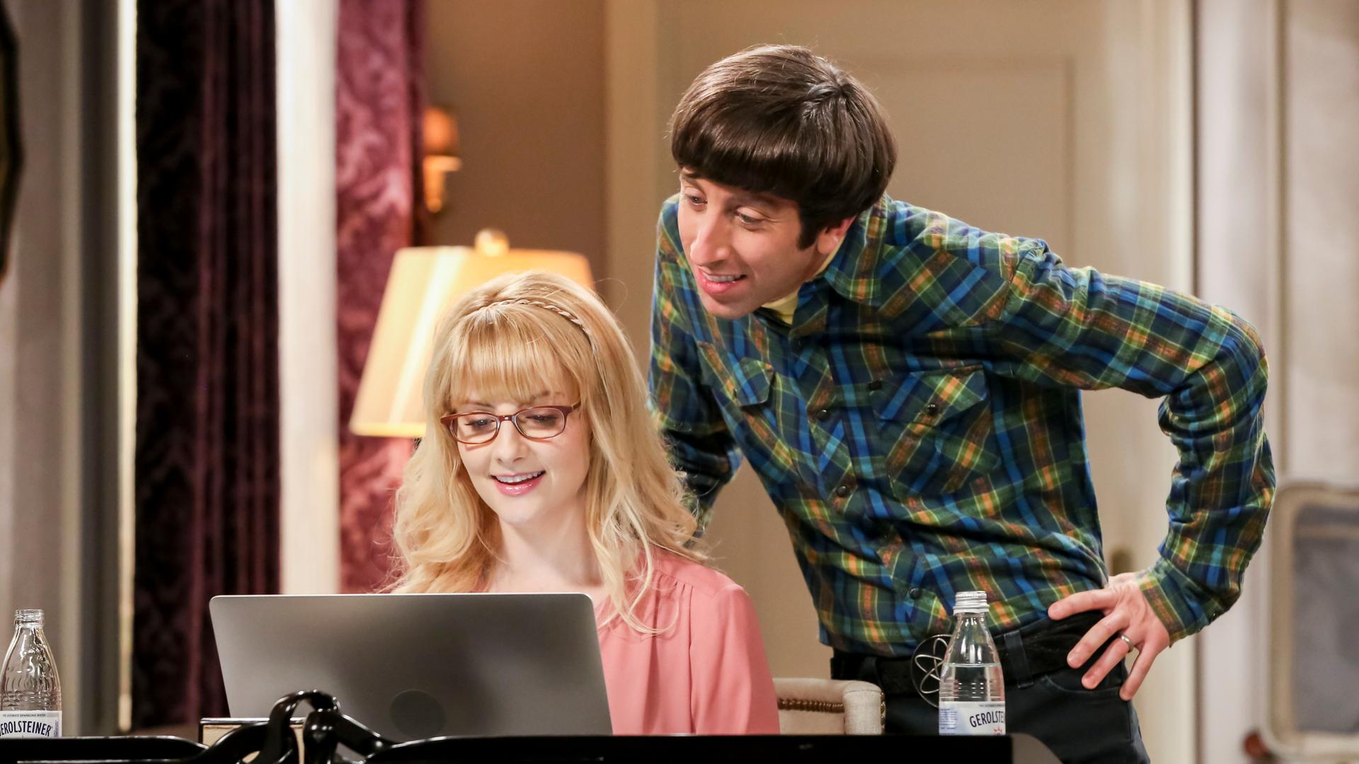 Ein Szenenfoto aus der US-TV-Serie "The Big Bang Theory". Es zeigt die Schauspielerin Melissa Rauch und den Schauspieler Simon Helberg. Sie sitzt am Laptop, er steht schräg hinter ihr.