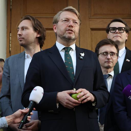 Nikolaj Rybakow steht umringt von Partei-Mitgliedern vor dem Gerichtsgebäude in Moskau und spricht in mehrere Mikrofone. In der Hand hält er einen grünen Apfel.