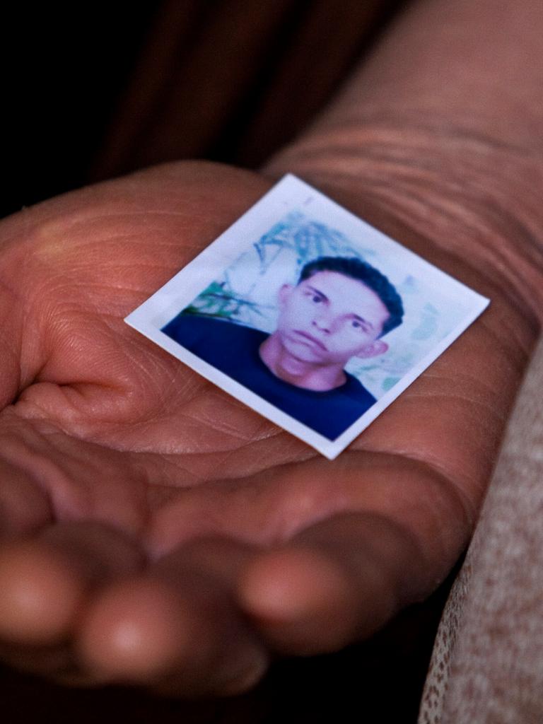 Nahaufnahme einer Frauenhand, die das Passfoto eines jungen Mannes in die Kamera hält. Er hat kurzes lockiges Haar und schaut ernst.
