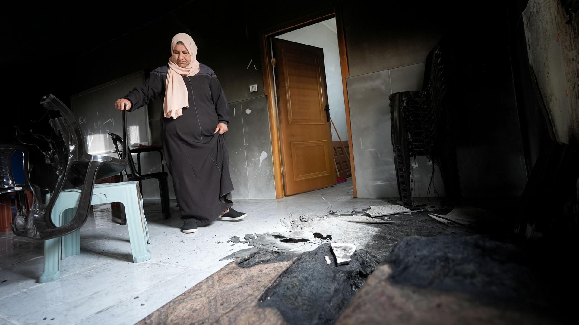 Eine Frau mit Kopftuch steht im Westjordanland vor Brandschäden in ihrem Zuhause. Siedler aus Israel hatten das Dorf Jibiya angegriffen.