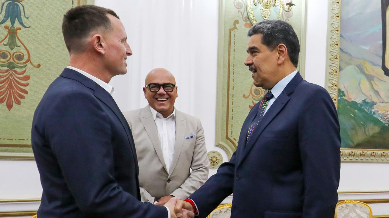 Grenell und Maduro in dunklen Jacketts geben sich die Hand. Dahinter lachend im hellen Jackett Rodriguez.