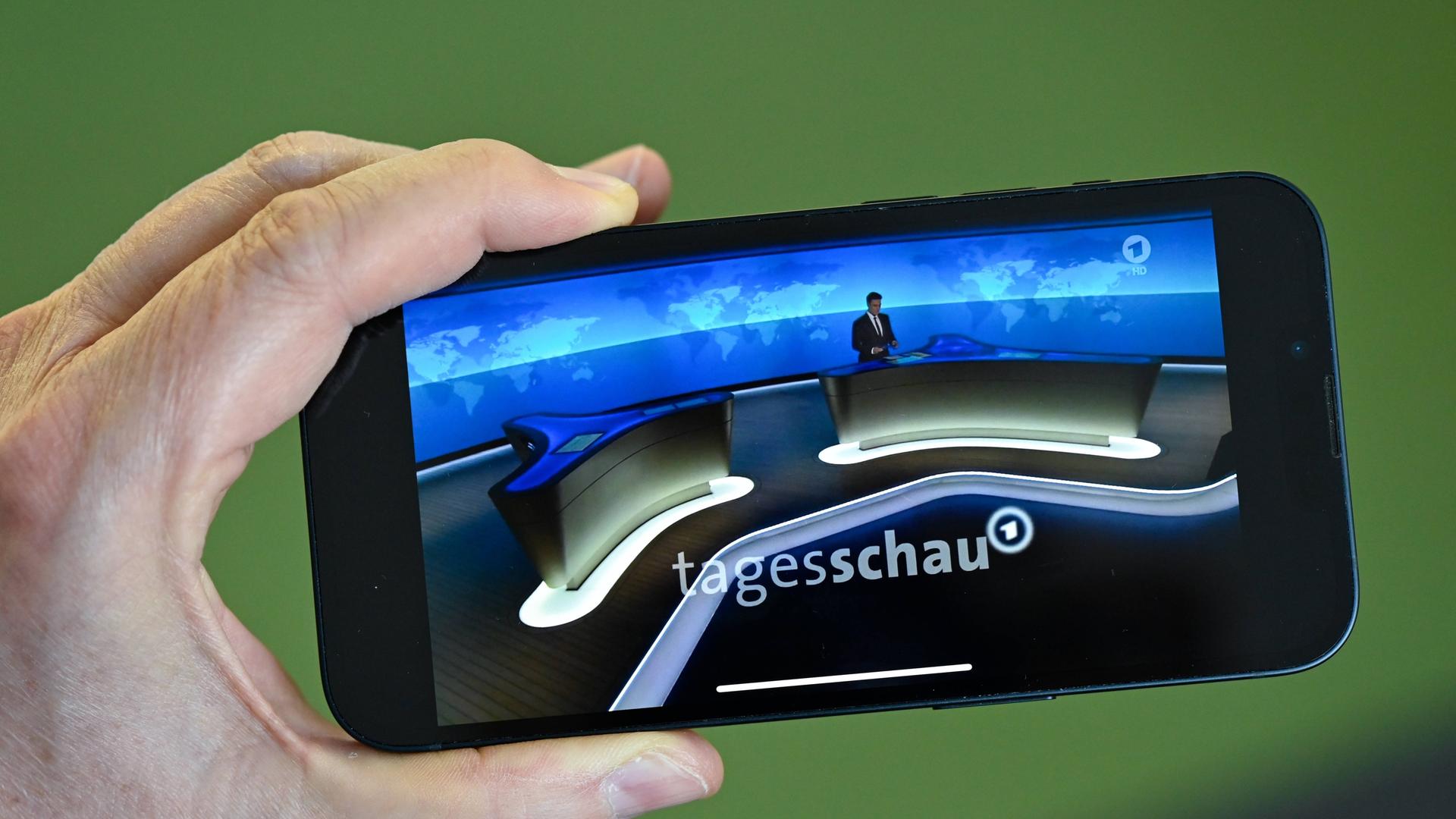 Ein Smartphone mit der Tagesschau-App wird von einer linken Hand gehalten.