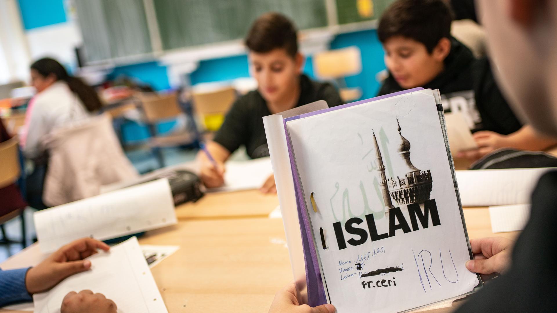 Schüler in einer Klasse, ein Schüler hält ein Unterrichtsbuch über den Islam in den Händen. 