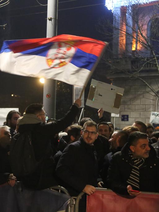 Protestierende schwenken die serbische Nationalflagge auf einer nächtlichen Straße.