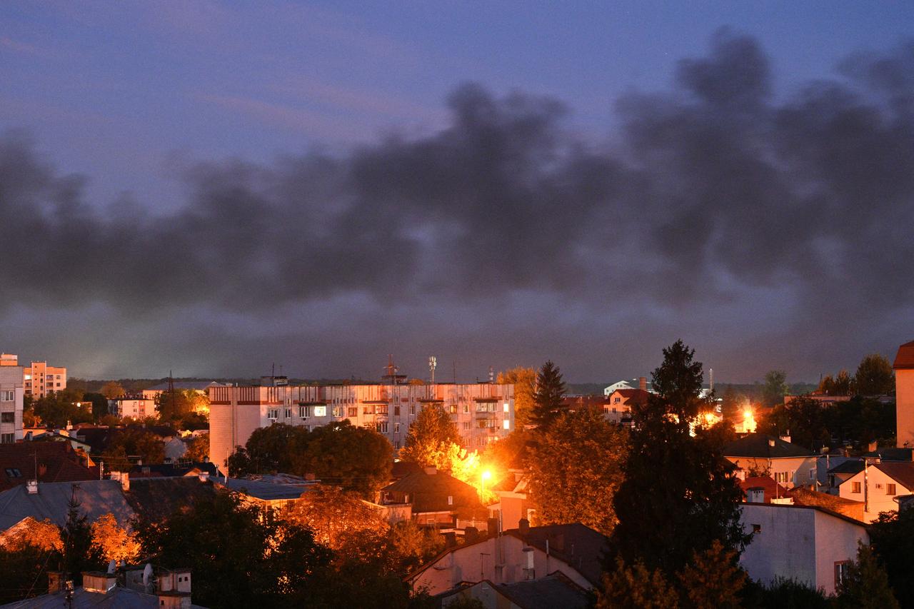 Blick auf die ukrainische Stadt Lwiw in der Dämmerung. Flammen schlagen aus einem Viertel, über der Stadt hängt dunkler Rauch.