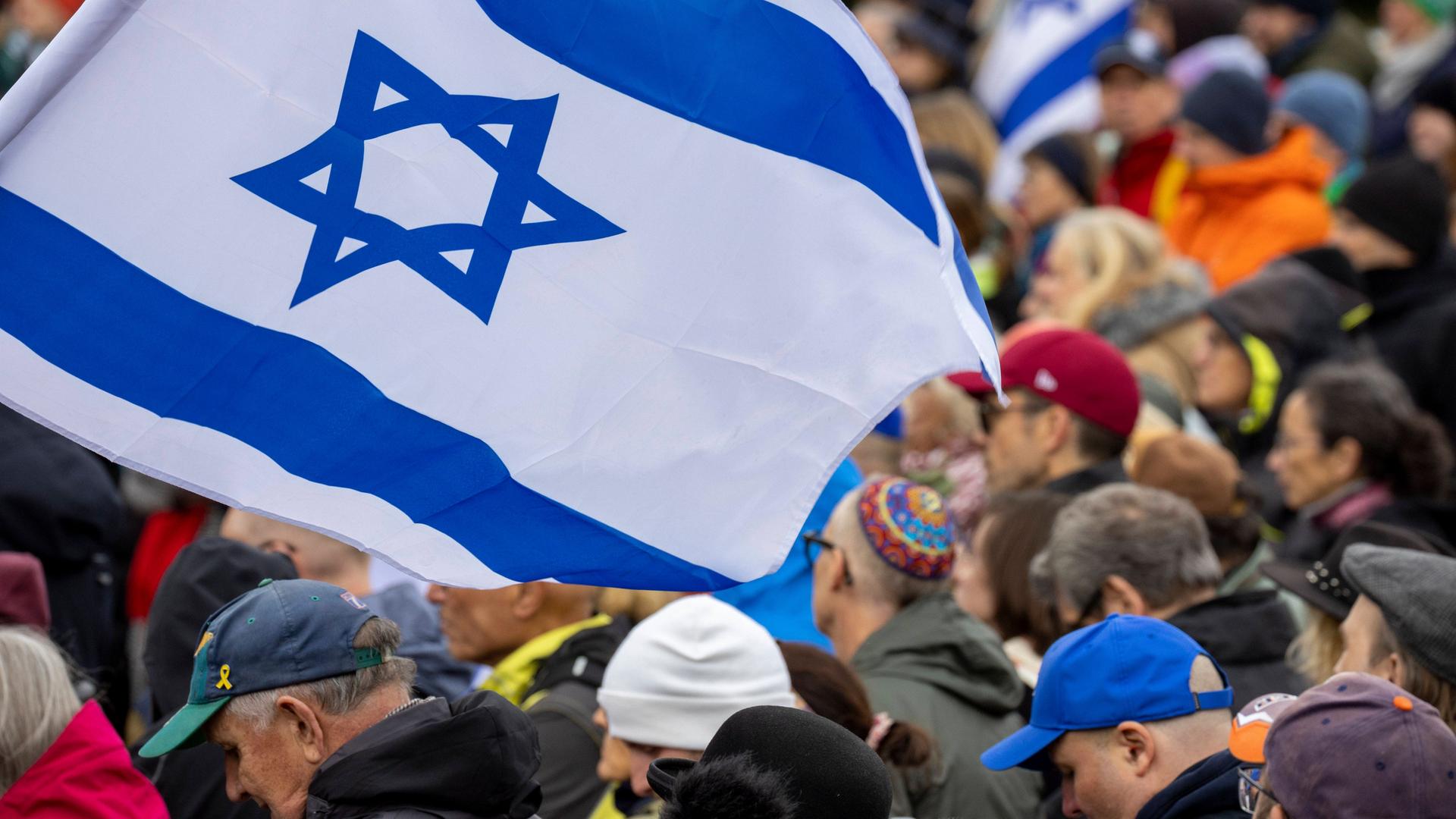 Menschen stehen nebeinander bei einer Kundgebung, einge tragen israelische Flaggen.