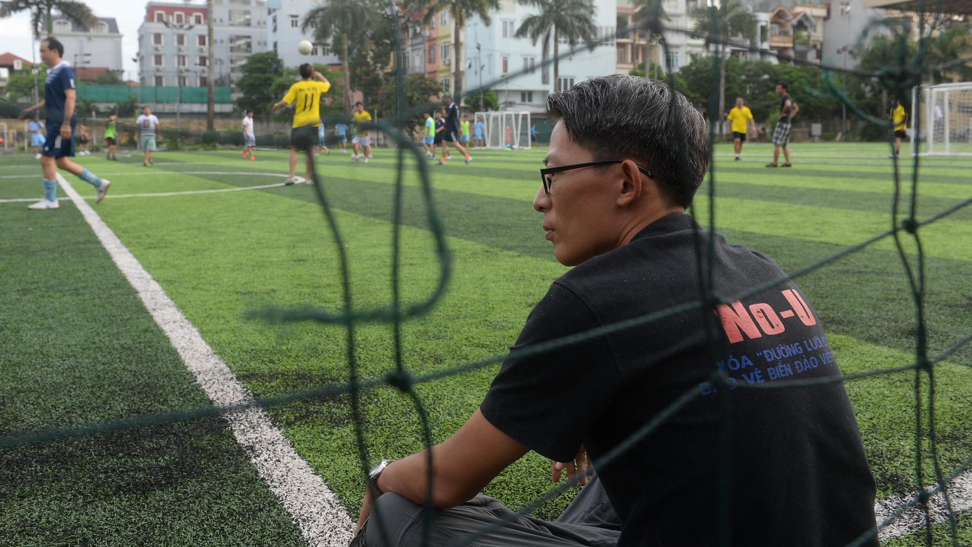 Der Blogger Nguen Lan Thang sitzt im Jahr 2017 am Rande eines Fußballfeldes in Hanoi und schaut einem Spiel zu.
