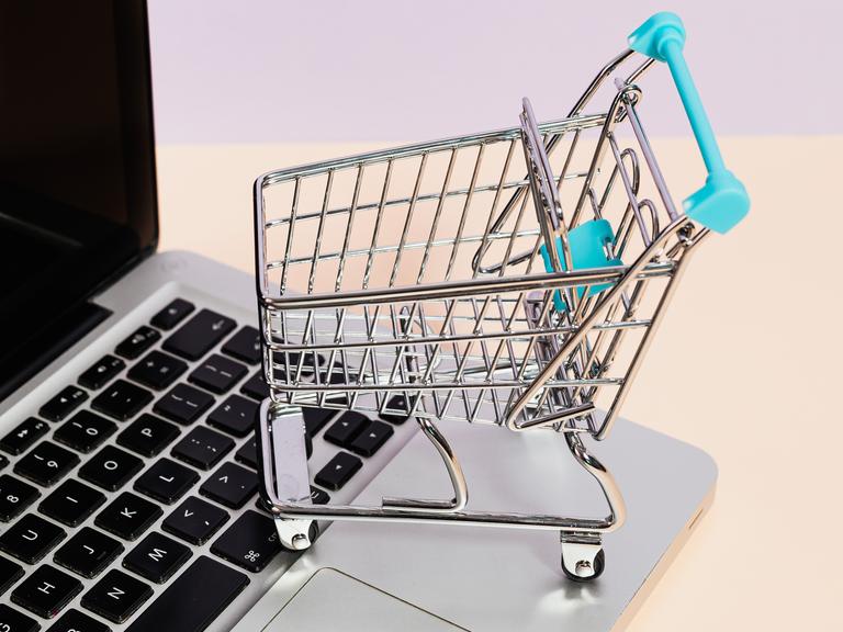 Ein Miniatur-Einkaufswagen steht auf der Tastatur eines Laptops.