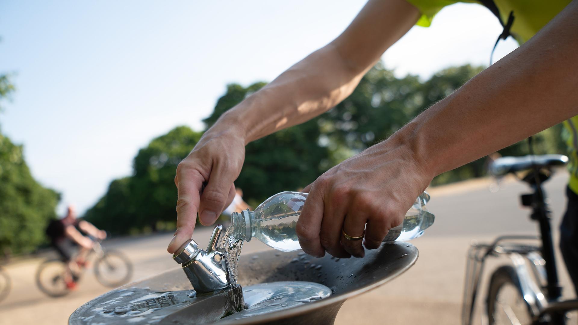 Ein Mann füllt an einem Trinkbrunnen seine Wasserflasche auf. Ein Mann füllt an einem Trinkbrunnen seine Wasserflasche auf.