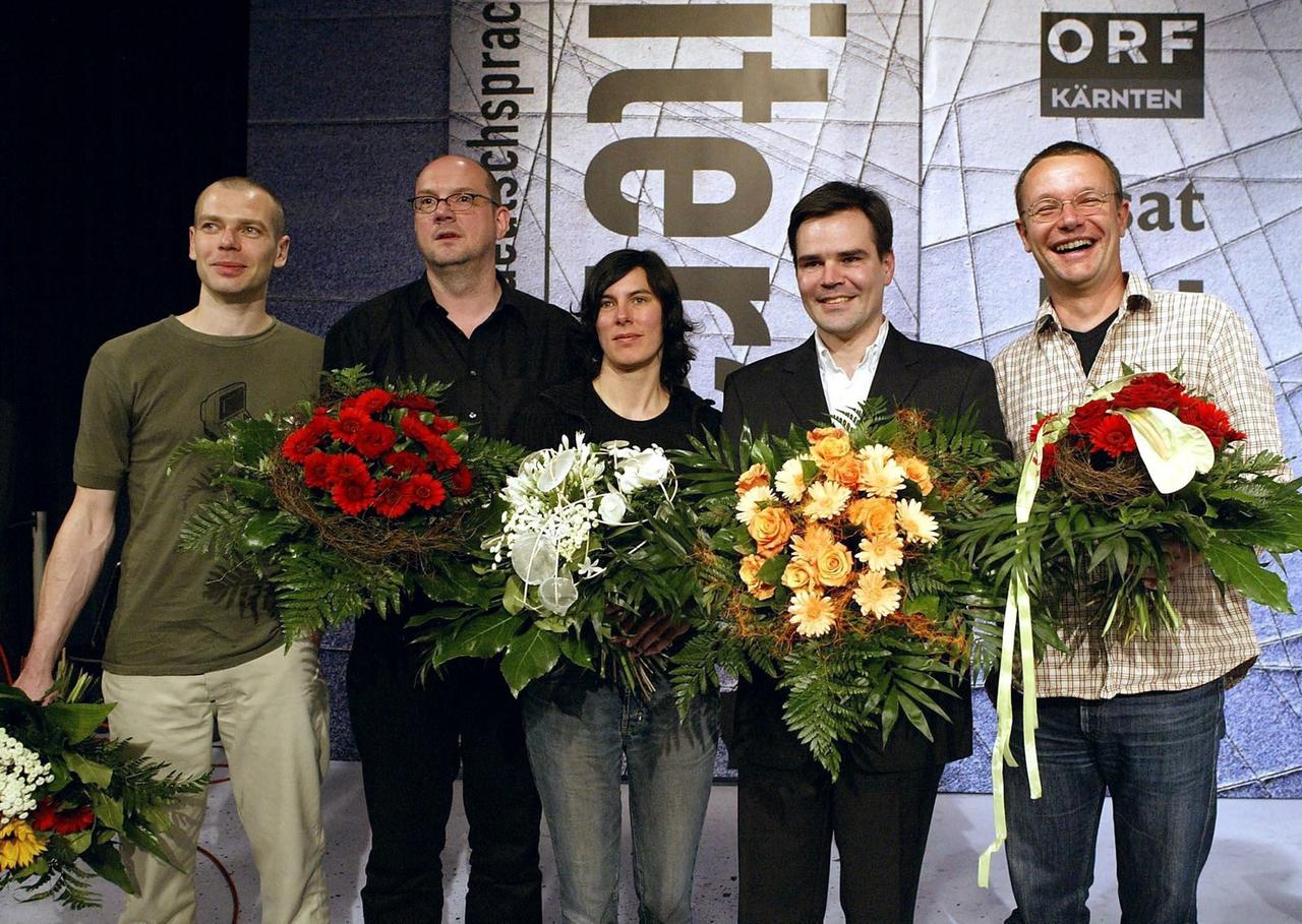 Bachmann-Preis 2004. Mehrere Personen stehen mit Blumen auf einer Bühne.