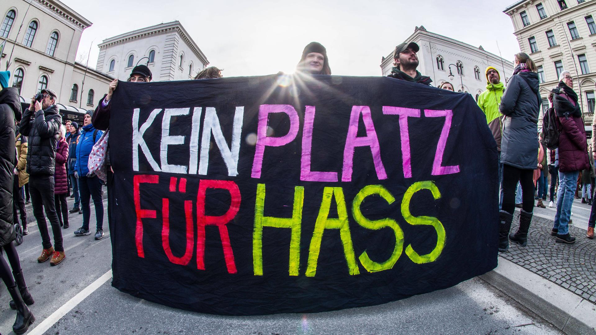 Ein Plakat auf einer Demo für die Demokratie in München wird gezeigt. Auf schwarzen Hintergrund steht in großen, bunten Lettern "KEIN PLATZ FÜR HASS".