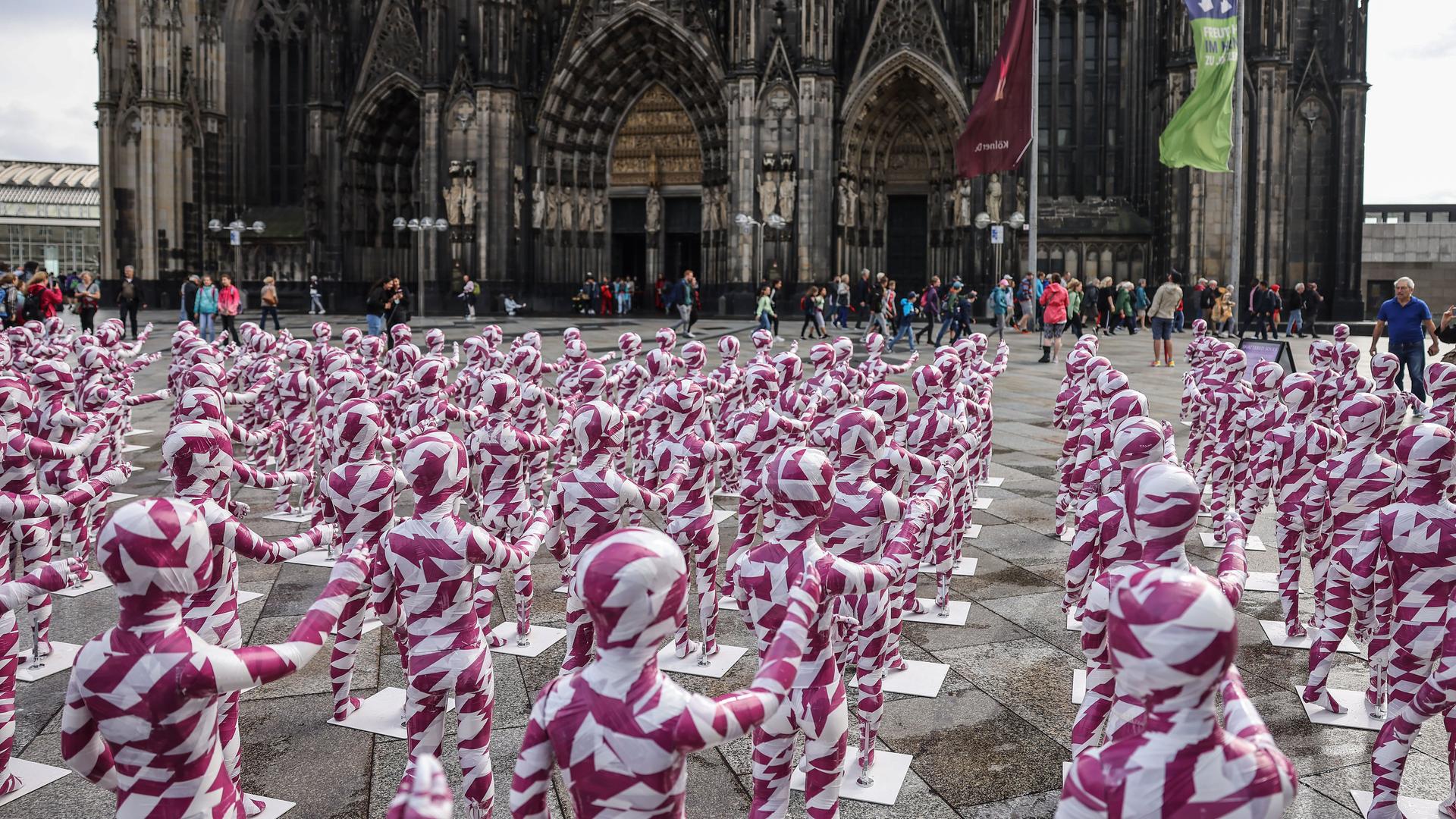 Die Installation "Shattered Souls ... in a Sea of Silence" steht auf dem Domplatz in Köln. Es sind 333 Kinderfiguren in rot-weiß getreiften Anzügen.